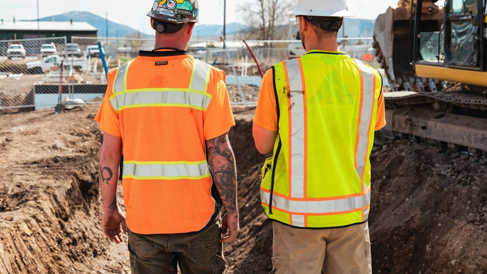 Two crew members in high-visibility vests checking an excavation on a job site