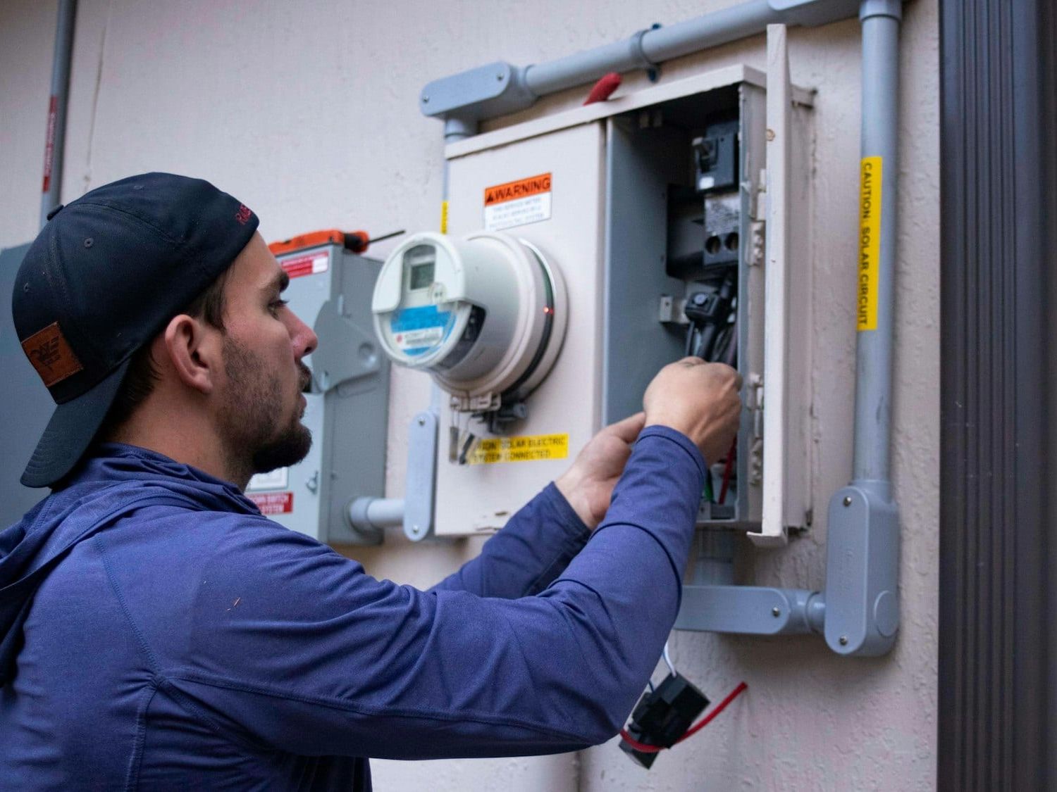Electrician working inside an outdoor meter and breaker panel