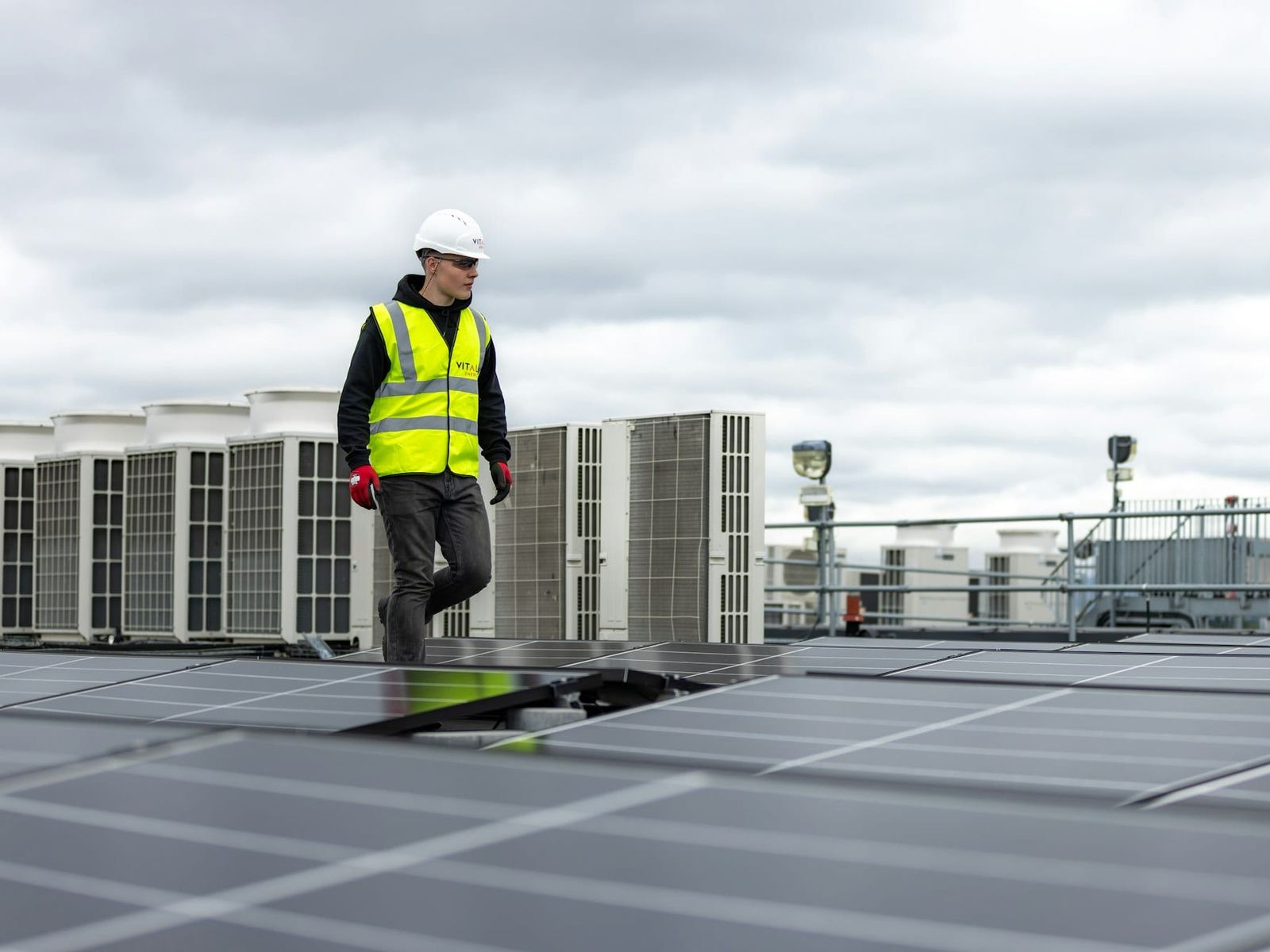 HVAC technician in a hard hat walking past rooftop units