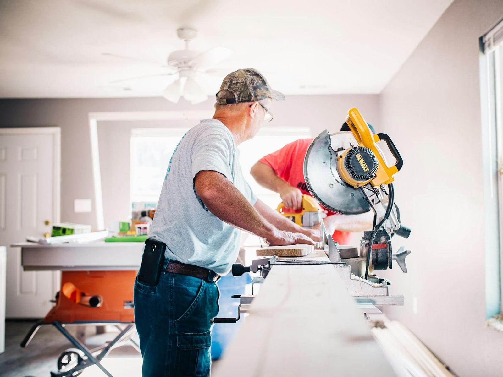 Two renovators cutting trim on a mitre saw inside a house