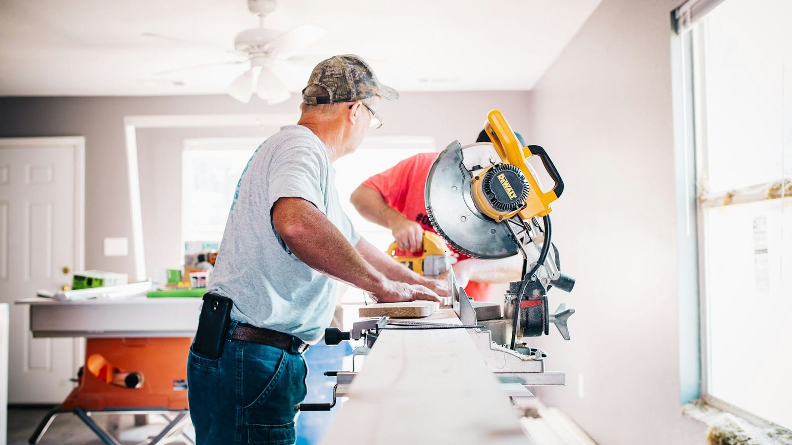 Two renovators cutting trim on a mitre saw inside a house