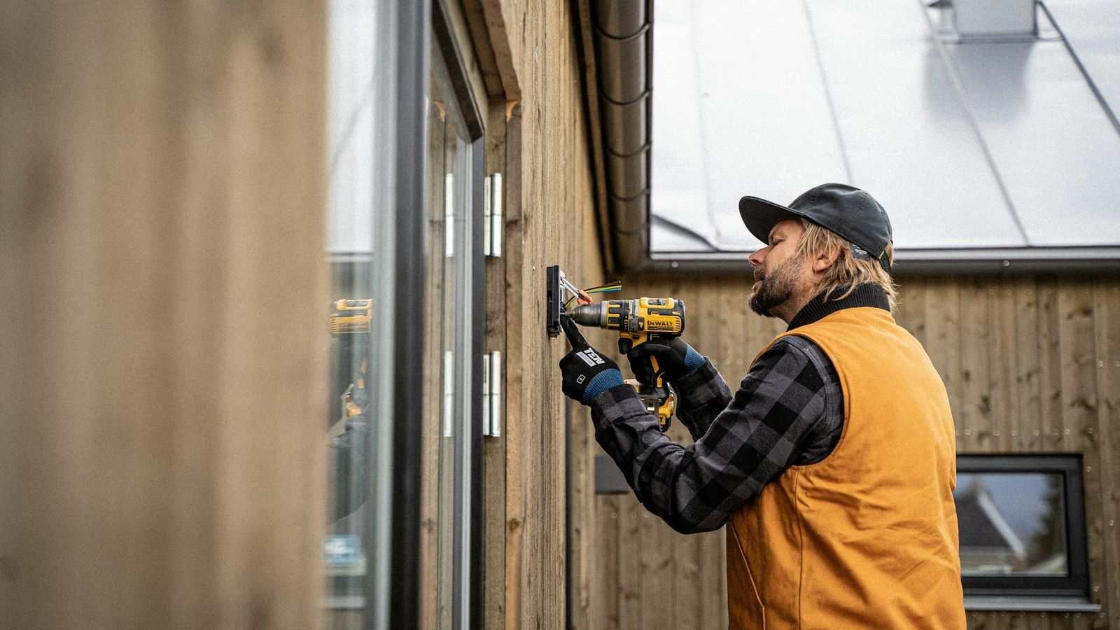 Tradesperson in a work vest drilling into an exterior wall